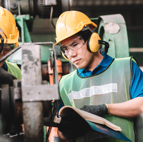 To ingeniører med sikkerhedshjelme, sikkerhedsbriller og høreværn på, der arbejder på en maskine.